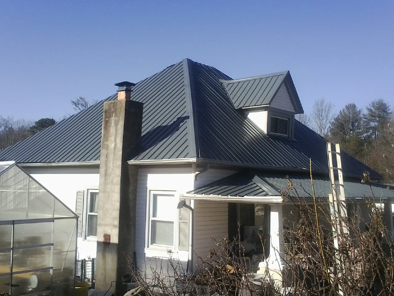 Dark blue standing seam metal roof on a white farmhouse with dormer — Slate & Tile Roof Repair by Roofing Brothers in Reevesville
