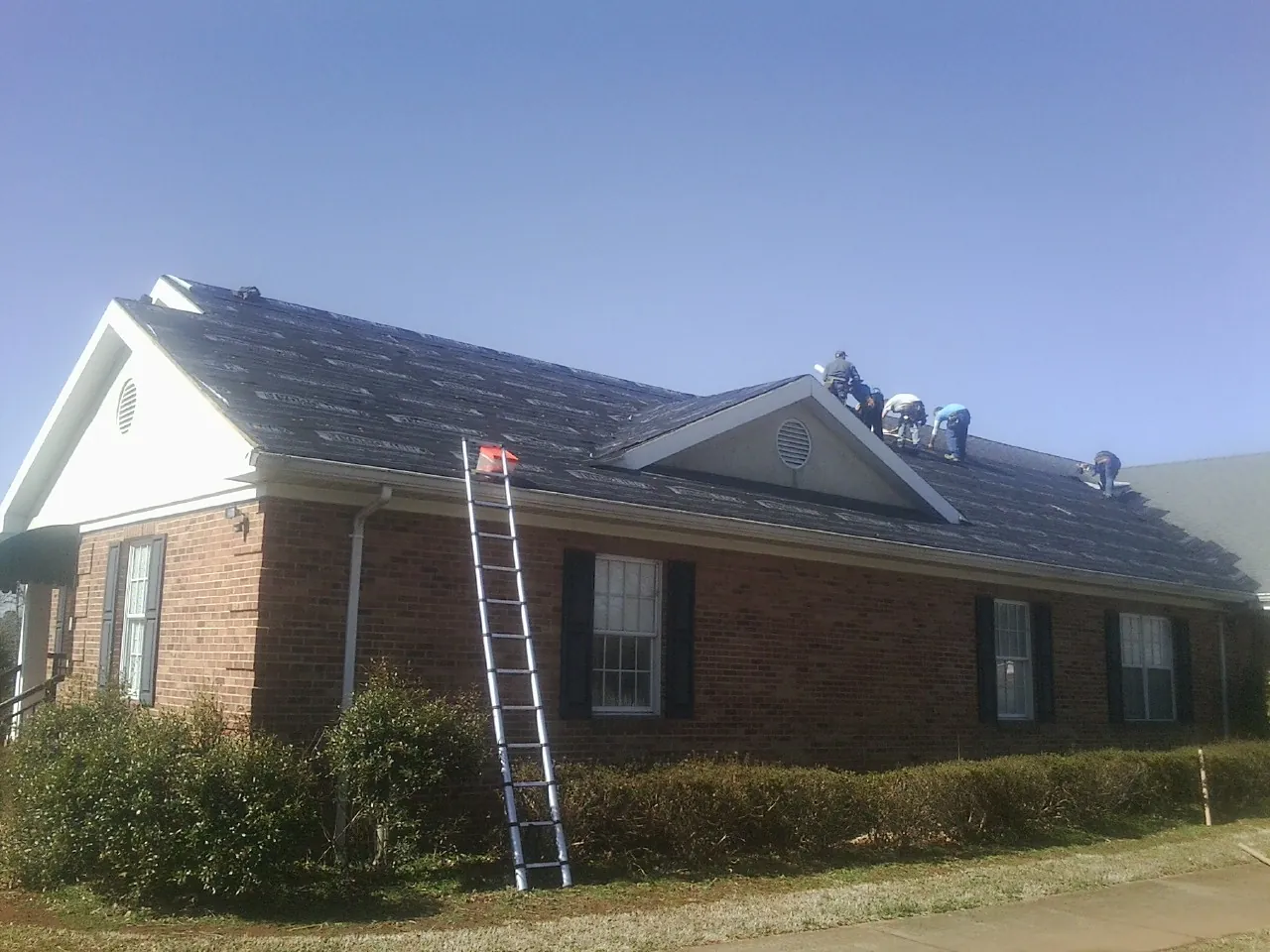 Crew tearing shingles off a brick ranch roof with a ladder set — Metal Roof Repair work by our crew in Reevesville