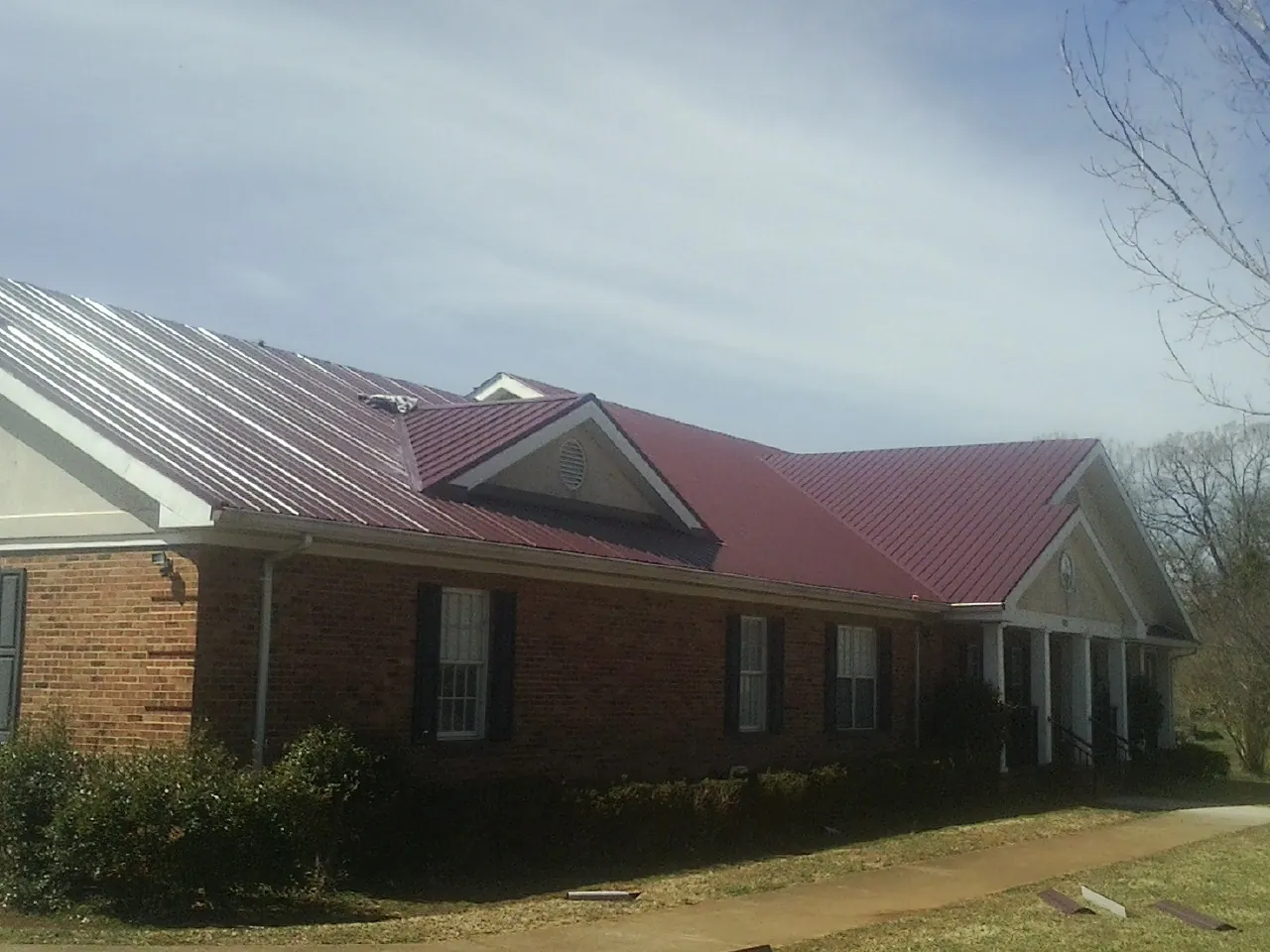 Red metal roof with gabled entries on a long brick building, from a Hail Damage Roof Repair job in Reevesville