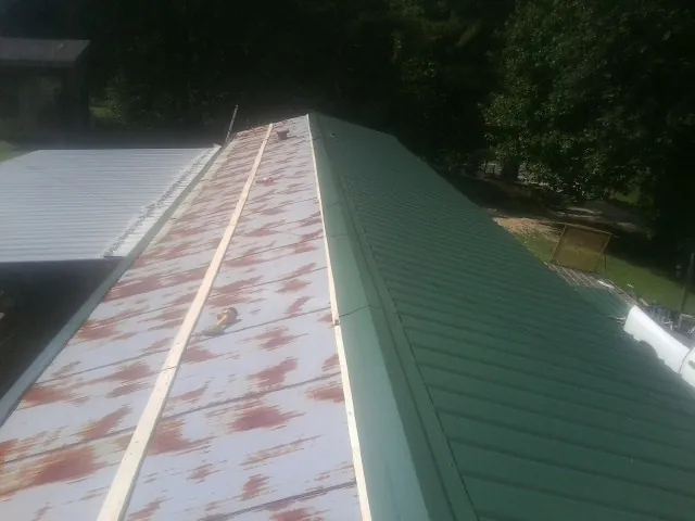 Old rusted panels beside newly installed green metal roofing — Wind Damage Roof Repair by Roofing Brothers in Reevesville