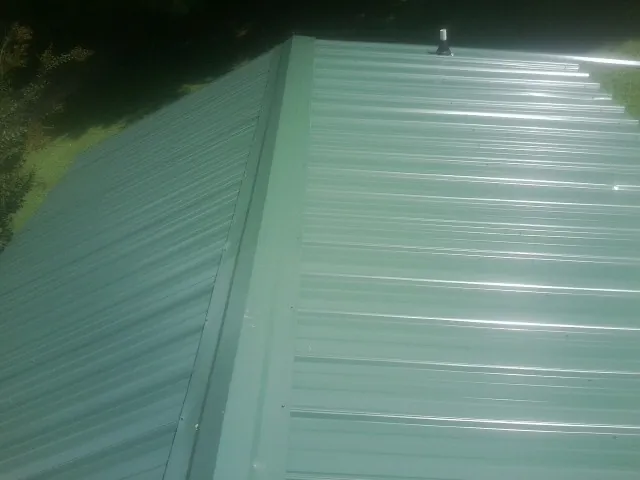 New green metal panels meeting at the ridge of a roof — Flat Roof Repair work by our crew in Reevesville