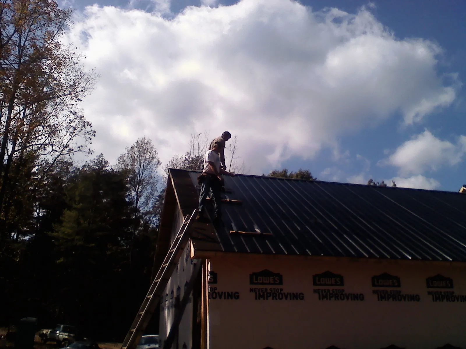 Roofer fastening dark metal panels high against a cloudy sky, from a Roof Inspection job in Reevesville
