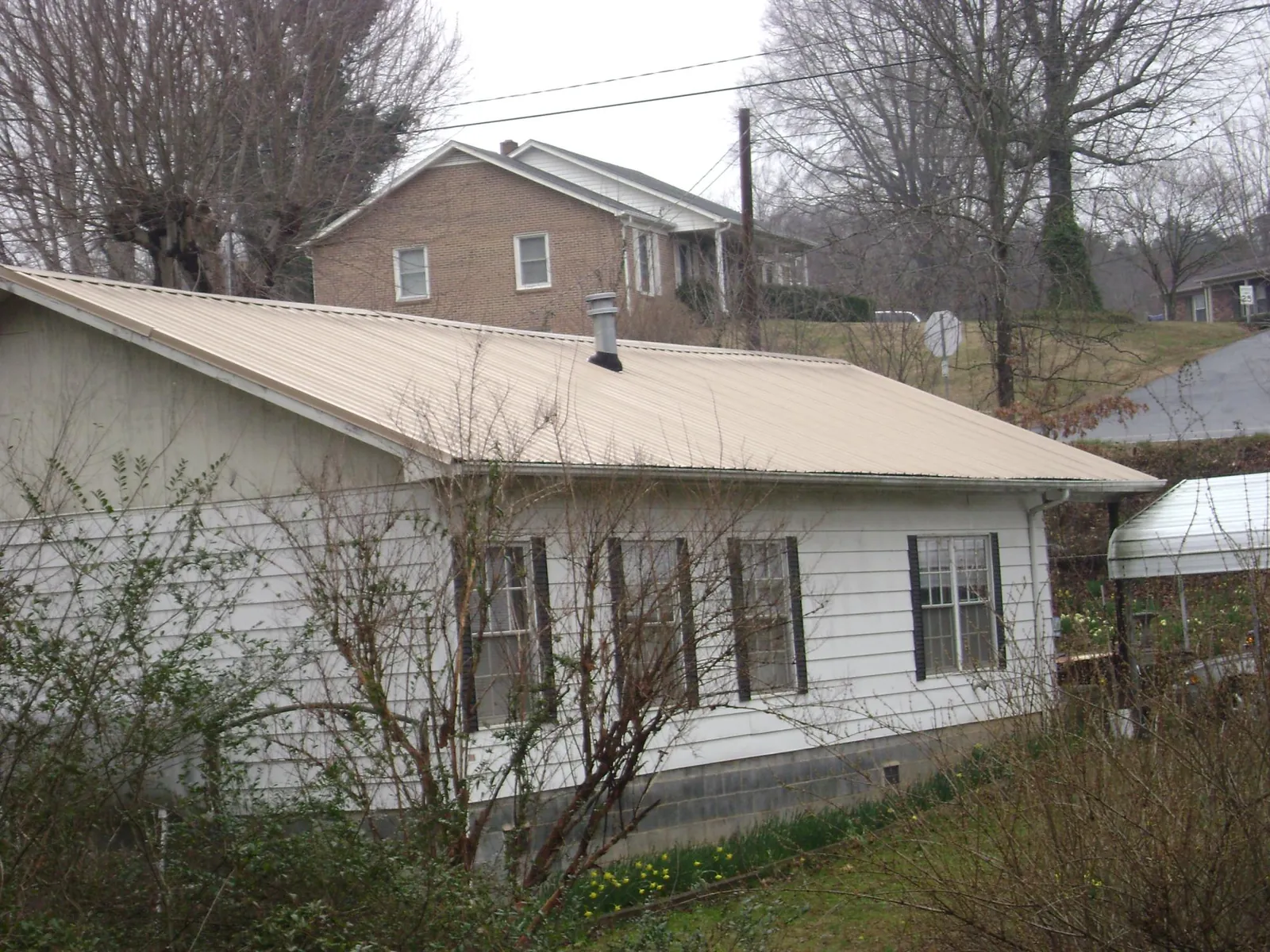 Tan metal roof on a white sided house set into a hillside — Commercial Roofing by Roofing Brothers in Reevesville