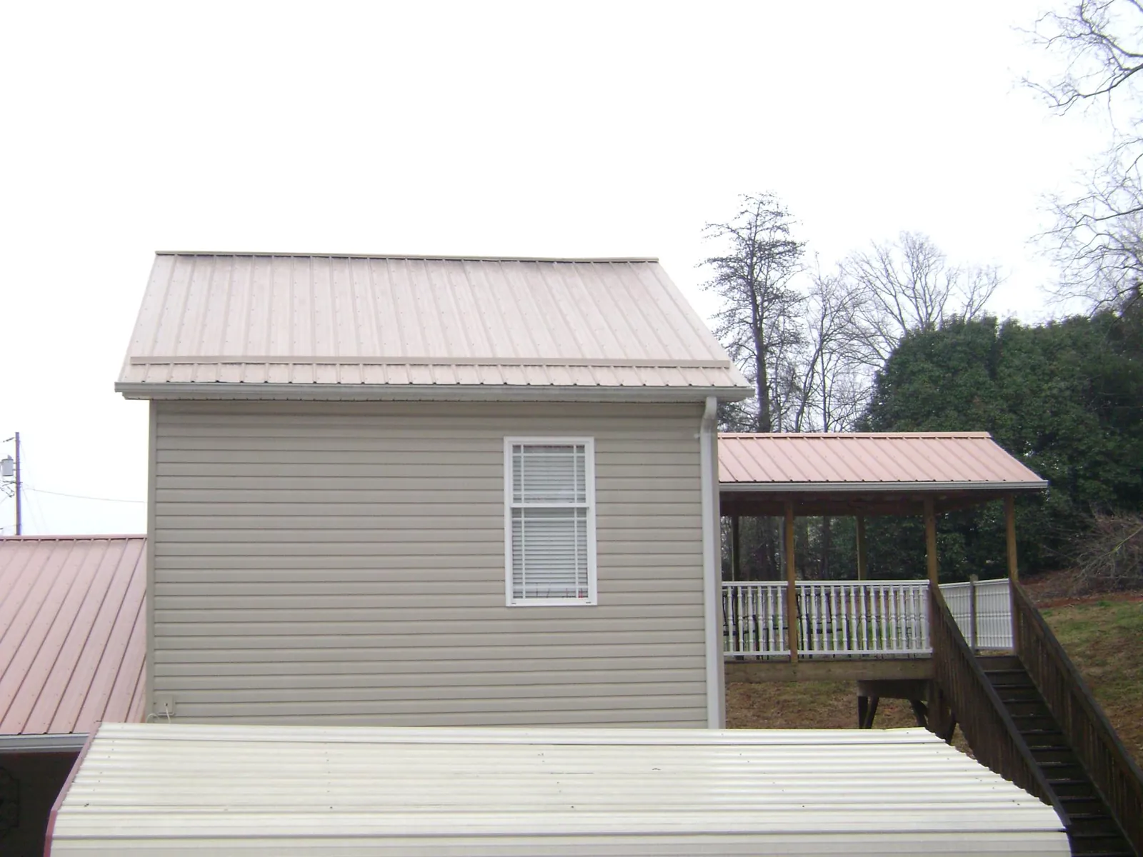 Tan metal roofs on a two story addition and attached porch, from a Roof Replacement job in Reevesville